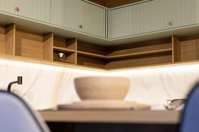 Detalhe de cozinha com armários verde sálvia, ripado em madeira e iluminação linear.